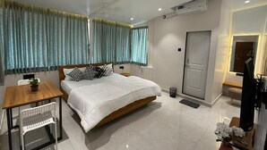 A modern hotel room with a large bed, a wooden desk, a small table, and a TV. - The Tranquo Stays (Alibag)