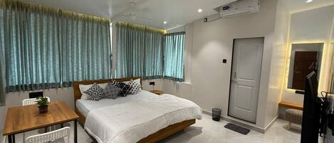 A modern hotel room with a large bed, a wooden desk, a small table, and a TV.