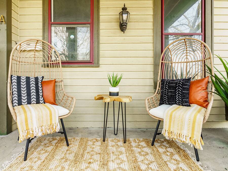 Two wicker chairs with cushions, a small table with a plant, and a potted plant beside the chairs.