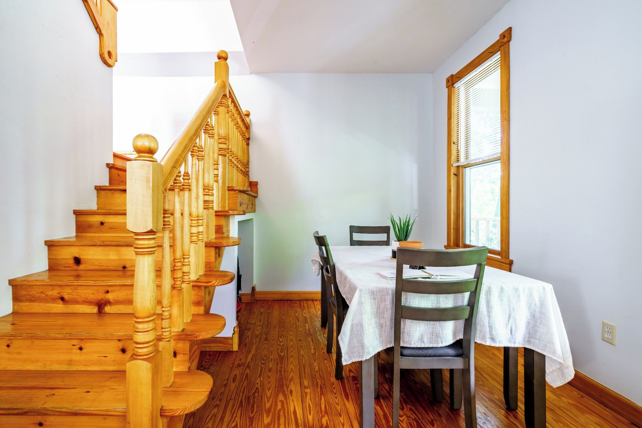 Un escalier en bois mène à un espace repas comprenant une table et des chaises.