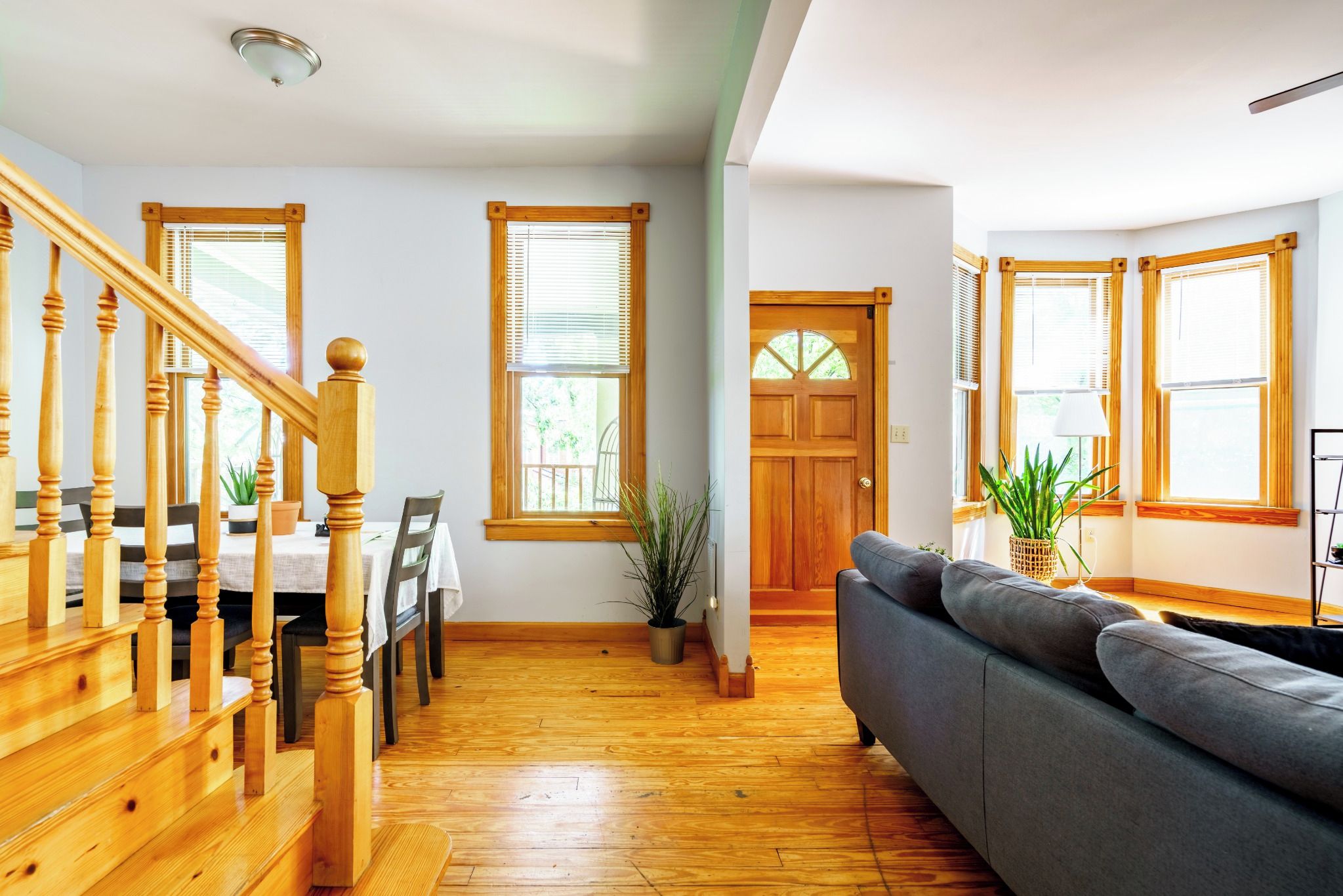 Un amplio espacio de estar con una escalera de madera, una mesa de comedor y un sofá gris.