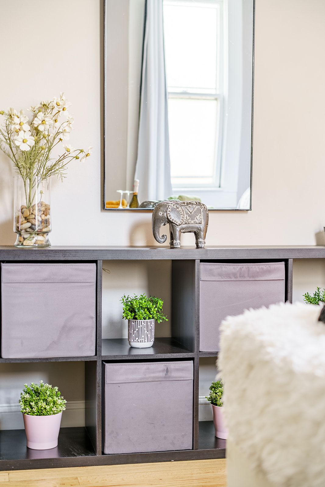 Una habitación con un espejo grande, una figurita decorativa de elefante y plantas en macetas sobre un mueble bajo oscuro.