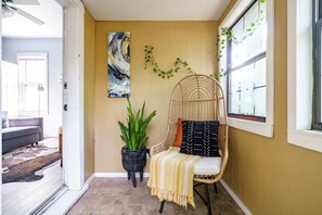 A room with a rattan chair, a potted plant, and a painting on the wall. - Jungle House Boutique Lofts – Downtown Columbus & Short North (Columbus)