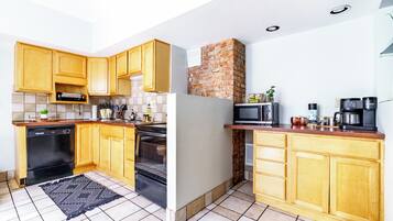 A compact kitchen with wooden cabinets, a microwave, a coffee maker, and a brick wall.
