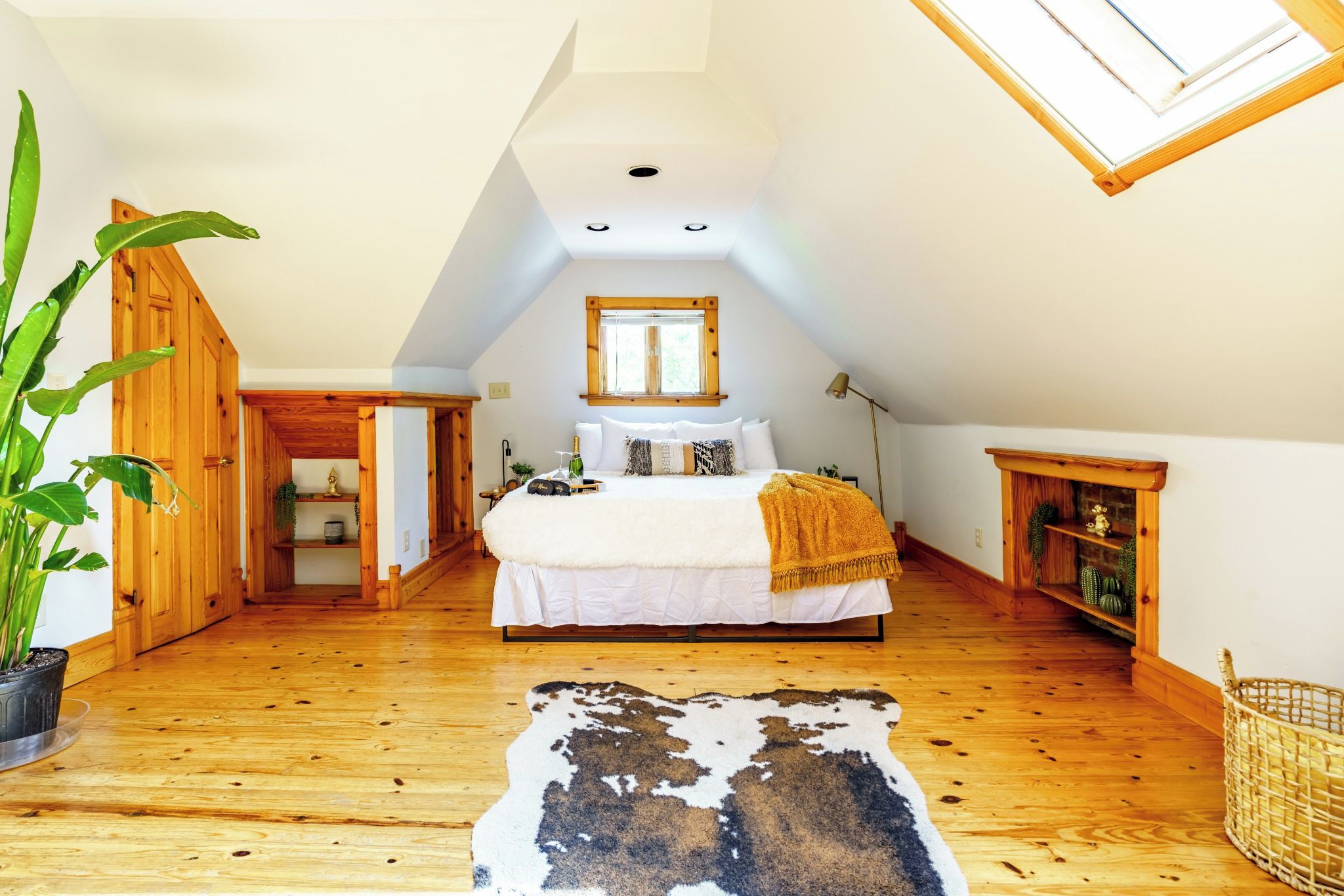 Une chambre avec un plafond en pente, un grand lit, un puits de lumière, un plancher en bois et un tapis en peau de vache.