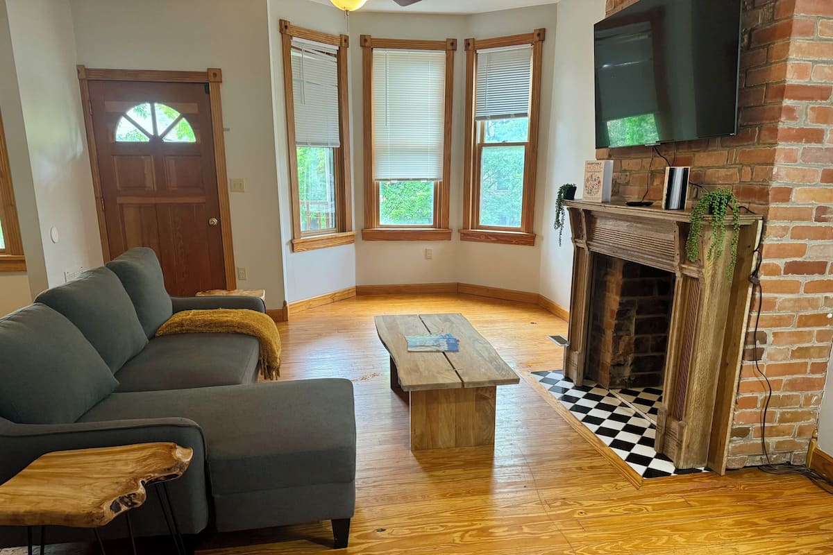A living room with a gray sofa, wooden coffee table, and a fireplace with a brick wall.