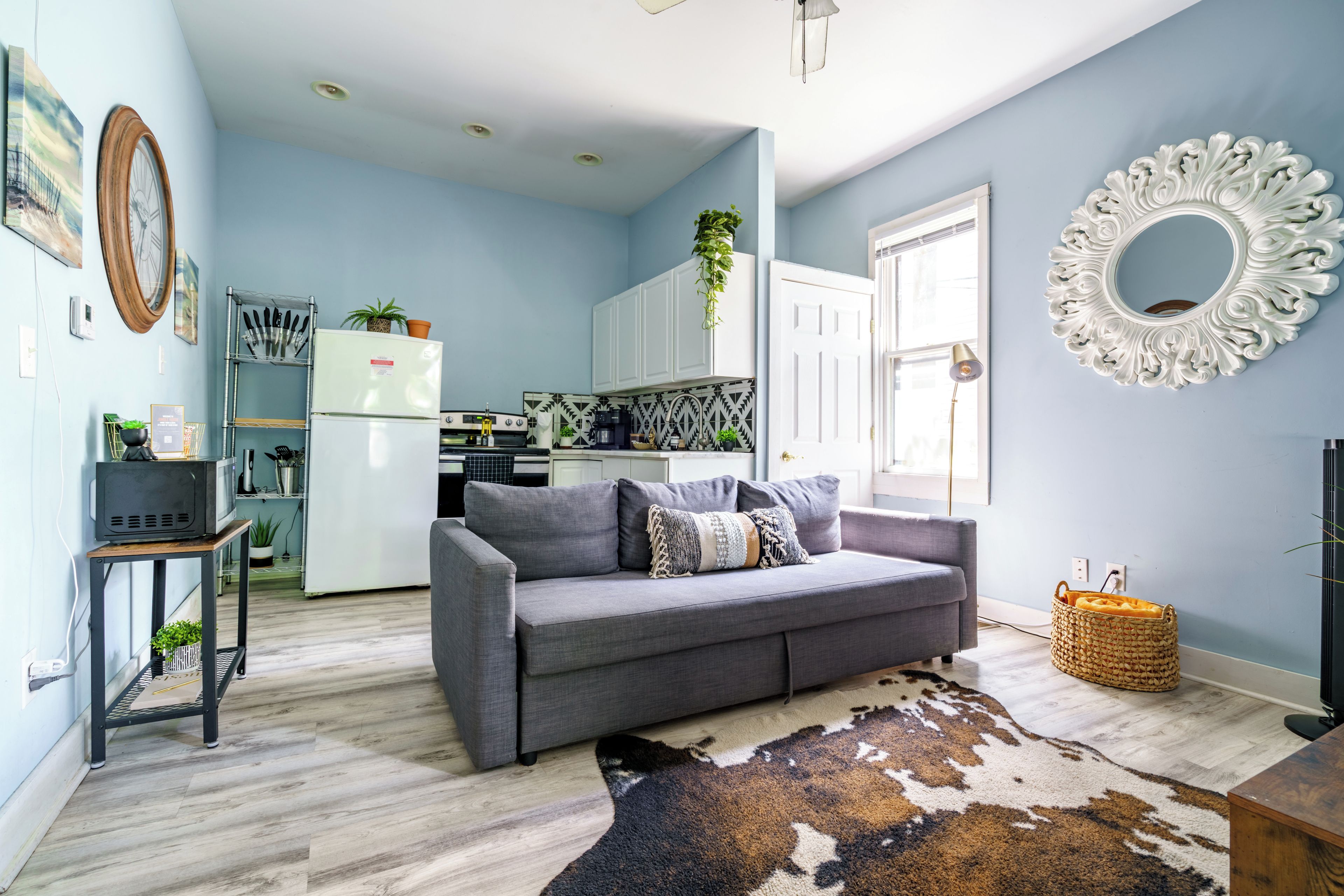 A modern living room with a grey sofa, a cowhide rug, and a kitchen in the background.
