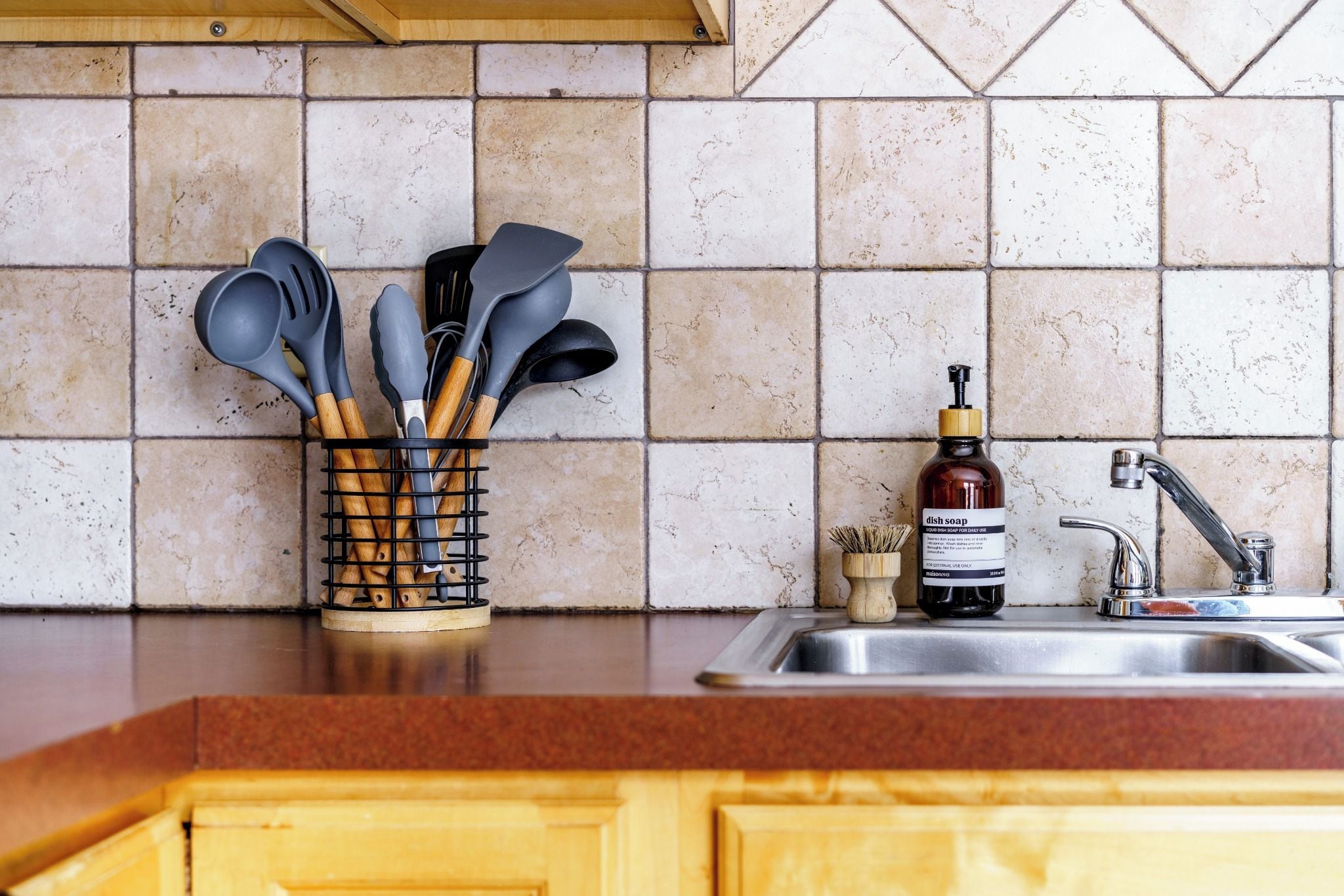 A kitchen with a sink, a dish soap bottle, and a utensil holder on the counter.