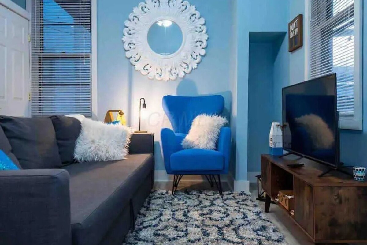 A living room with a blue armchair, a grey sofa, a TV, and a decorative mirror on the wall.