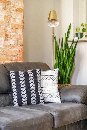 A grey sofa with patterned cushions, a tall floor lamp, and a green plant. - Jungle House Boutique Lofts – Downtown Columbus & Short North (Columbus)