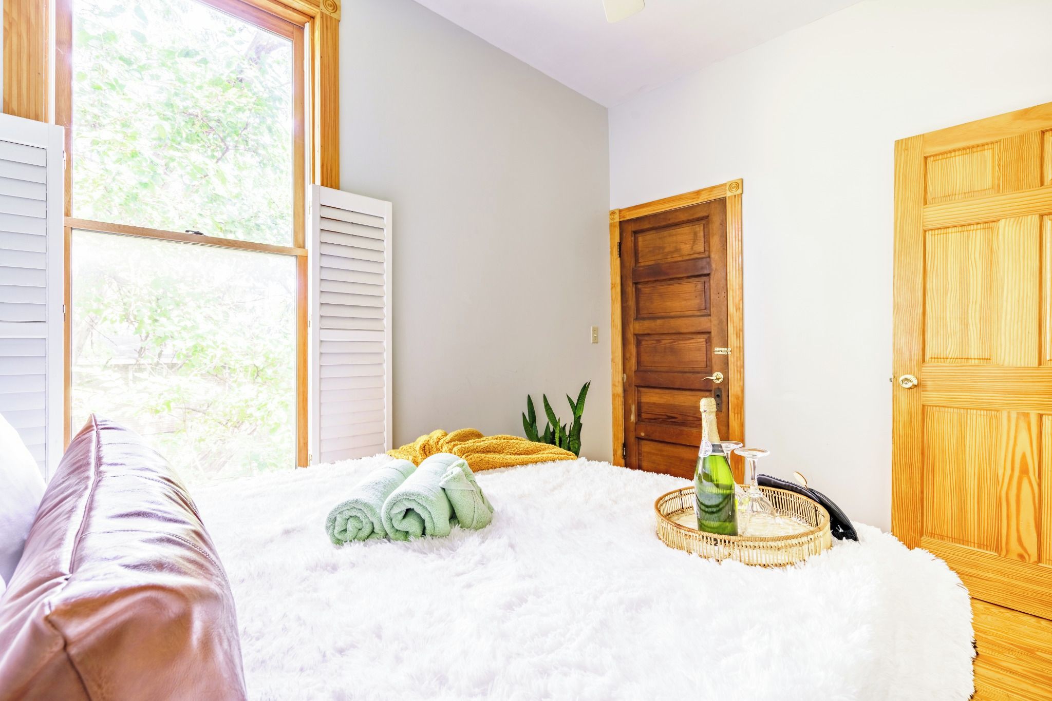 A bedroom with a bed, a window, a door, and a bedside table with a bottle and glasses.