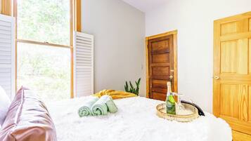 A bedroom with a bed, a window, a door, and a bedside table with a bottle and glasses.
