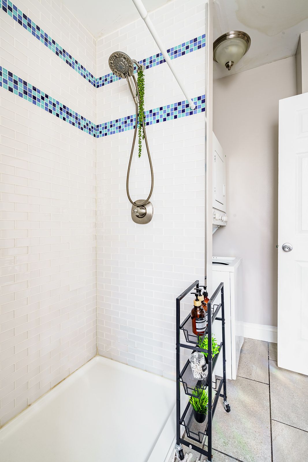 Een badkamer met een douche, witte betegelde wanden, een witte badkuip en een metalen rek met toiletartikelen.
