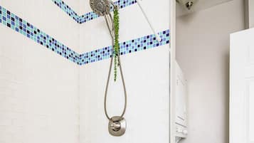 Een badkamer met een douche, witte betegelde wanden, een witte badkuip en een metalen rek met toiletartikelen.