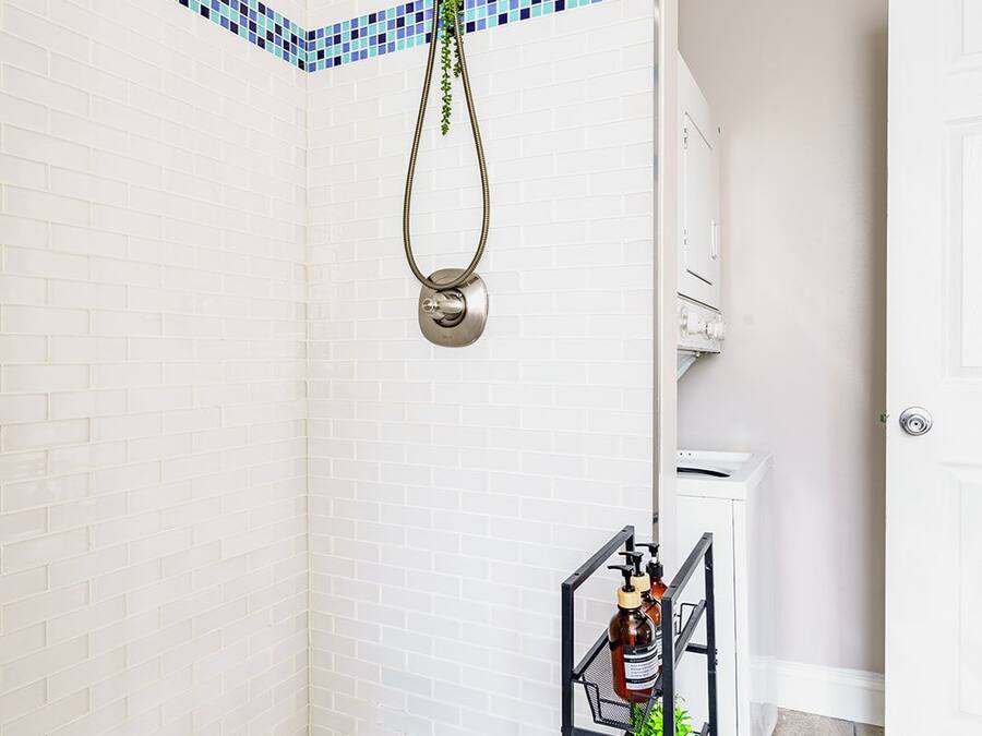 A bathroom with a shower, white tiled walls, a white bathtub, and a metal rack with toiletries.
