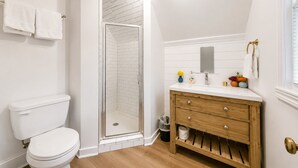 A bathroom with a toilet, a shower with glass doors, a vanity with a mirror, and a window. - Jungle House Boutique Lofts – Downtown Columbus & Short North (Columbus)