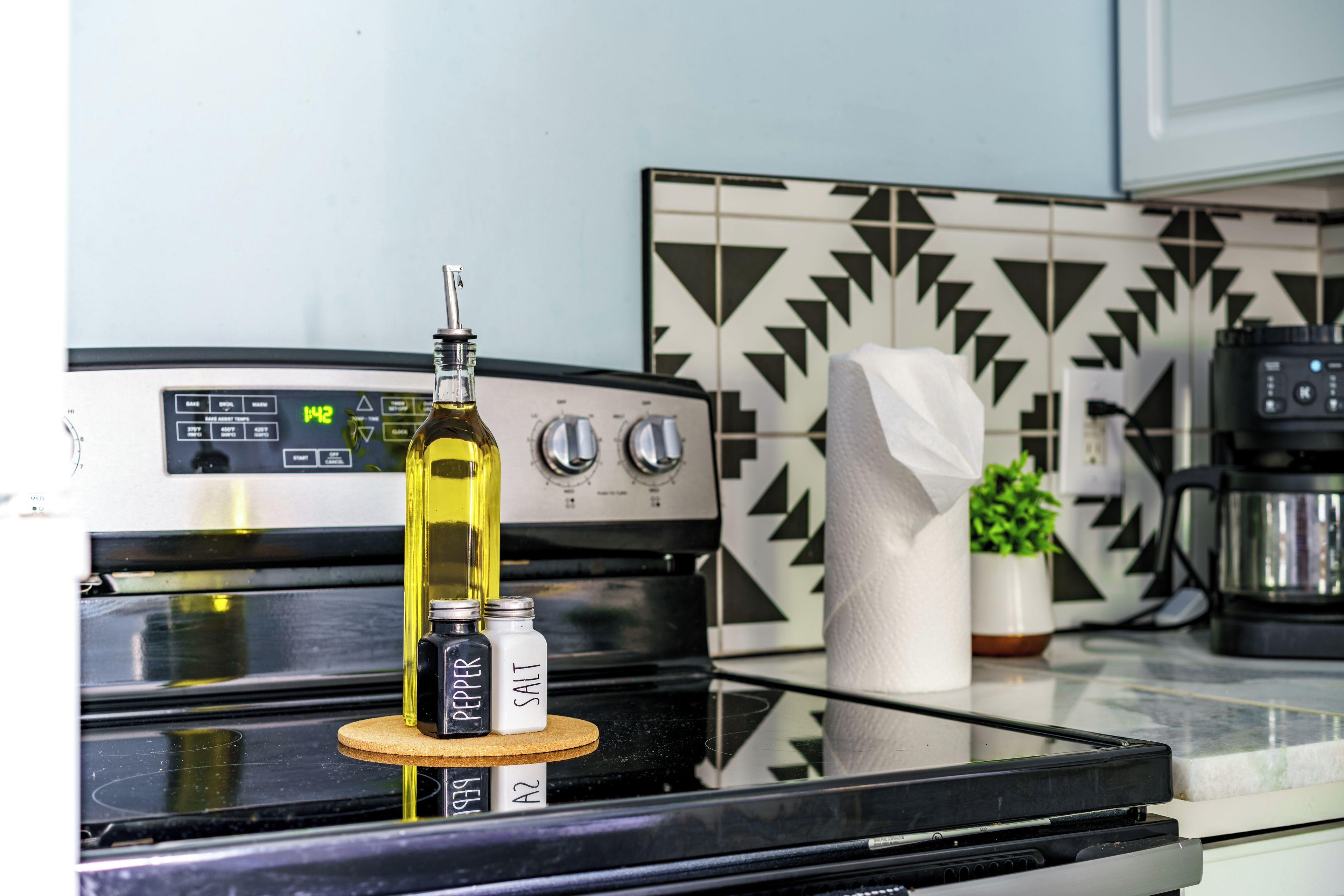 A kitchen with a stove, a bottle of olive oil, and a pepper grinder on the counter.