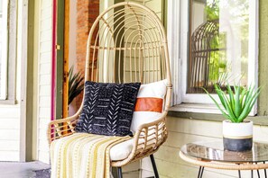 A wicker chair with a cushion and a throw blanket, positioned next to a window with a view of greenery. - Jungle House Boutique Lofts – Downtown Columbus & Short North (Columbus)