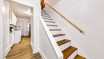 A modern interior with a staircase leading to a second floor, a kitchen area with white cabinetry, and wooden flooring.