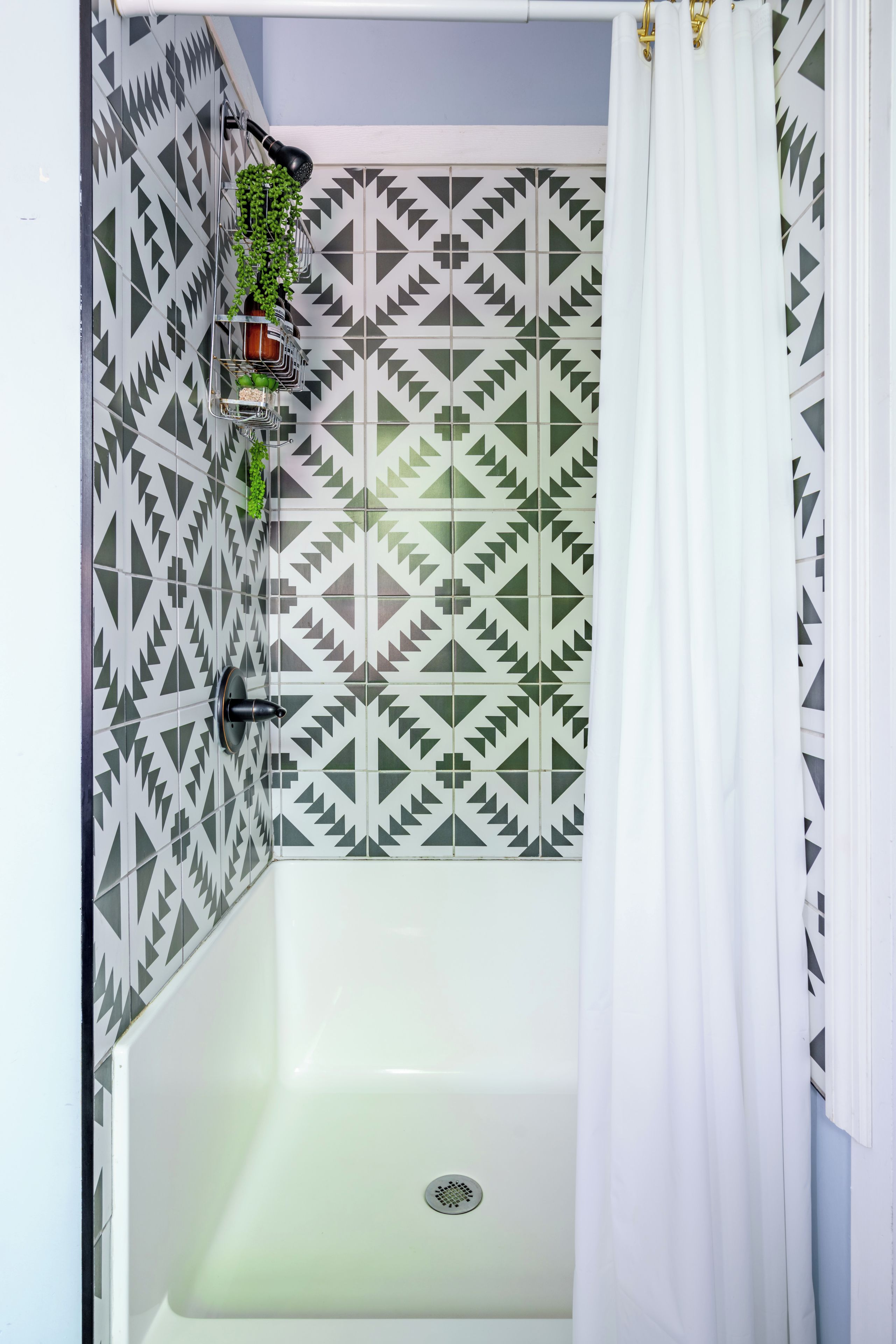 Un baño con pared de azulejos de diseño geométrico, una cortina de ducha y una planta en una cesta metálica.