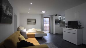 Una habitación de hotel moderna con cama, sofá, televisor y kitchenette.