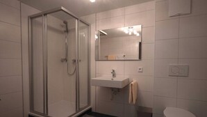 Un baño moderno con ducha de vidrio, lavamanos con toalla y retrete.