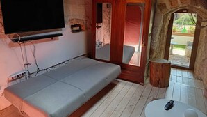 A cozy room with a bed, a TV mounted on the wall, a wooden door, and a small table with a remote control. - Borgo Incanto (Acquaviva delle Fonti)