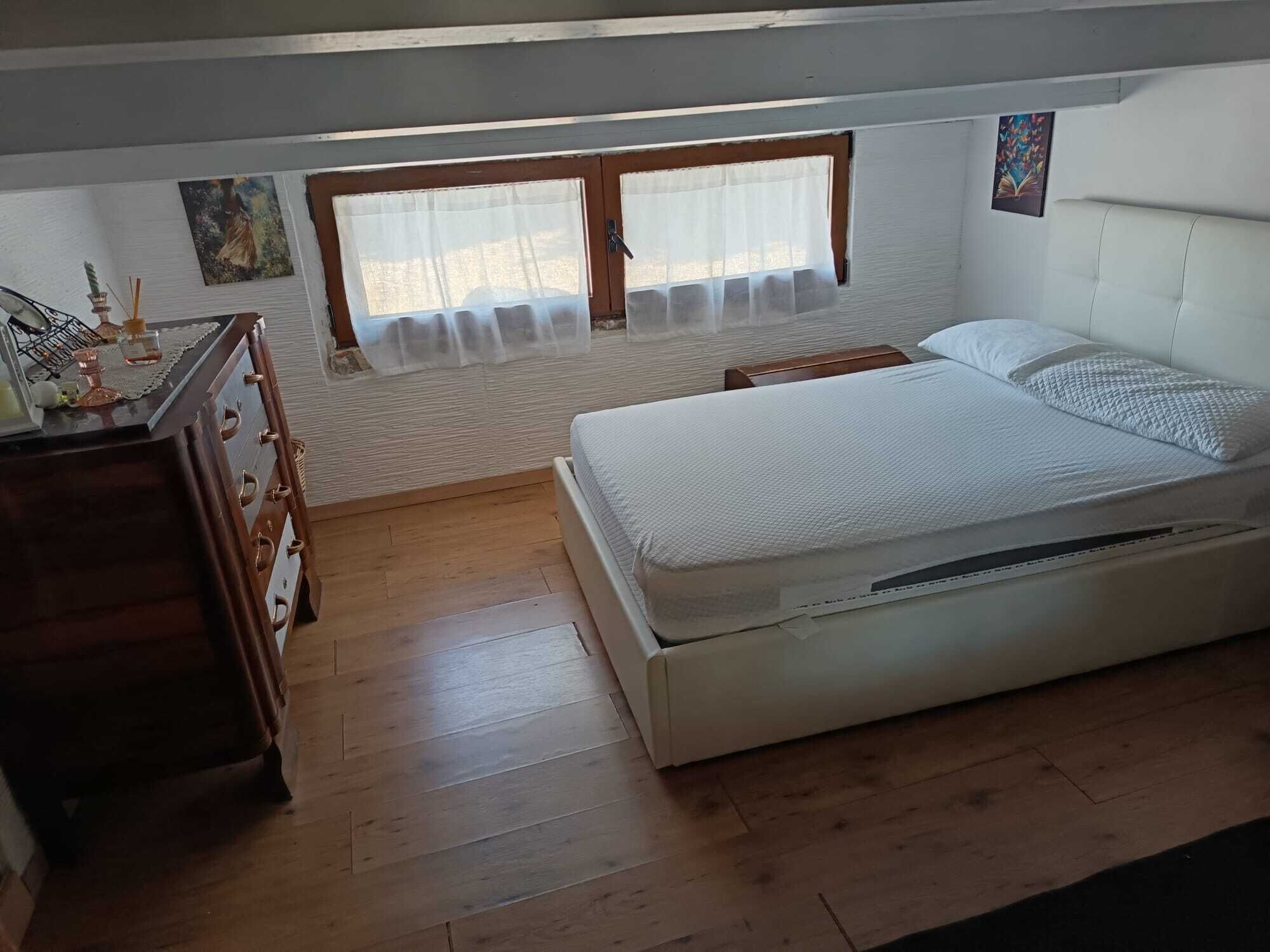 Une chambre à coucher avec un lit, une commode en bois et une fenêtre ornée de rideaux légers.