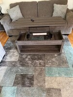 Una sala de estar con un sofá marrón, una mesa de centro de madera y una alfombra estampada.