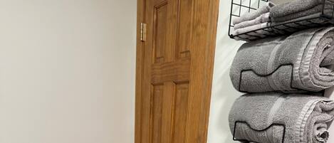 A bathroom with a wooden door, a toilet, and a towel rack with folded towels.