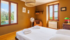 Ein Schlafzimmer mit Bett, Ventilator, Stuhl, Heizkörper und einem Fenster mit Aussicht.