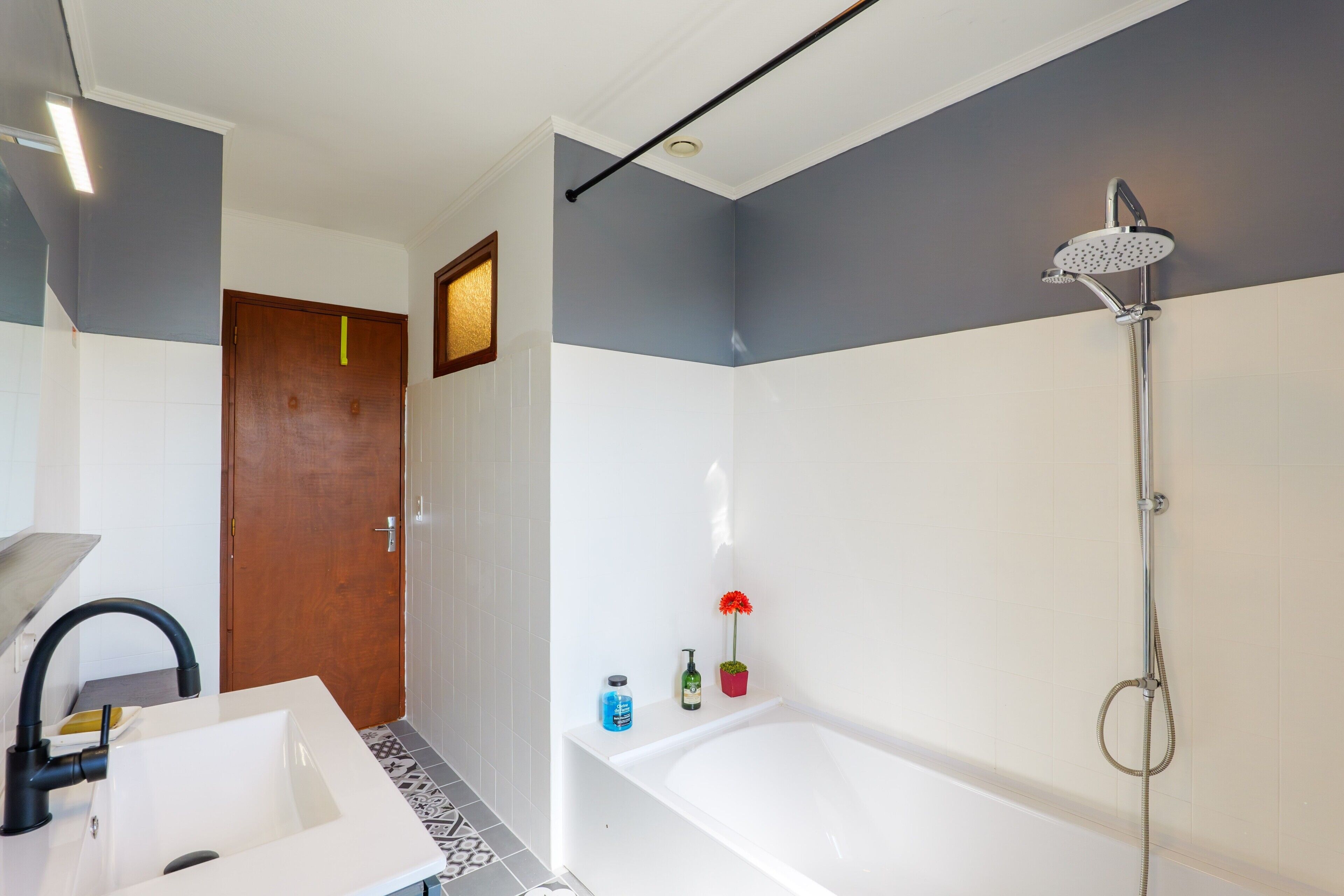 Un baño con lavamanos blanco, ducha con cabezal de ducha de mano y puerta con marco de madera.