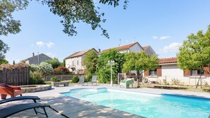Ein Schwimmbecken mit Liegestühlen, einer Steinterrasse und Häusern im Hintergrund.