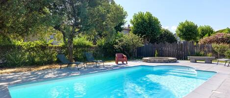 A rectangular swimming pool with a wooden deck surrounding it, a wooden fence, and a few trees.