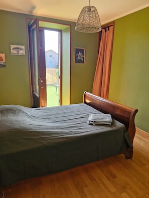 Een slaapkamer met een bed, een houten hoofdbord, een hanglamp en een deur naar een buitenruimte.
