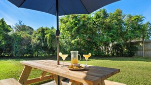 Une table de pique-nique en bois, un parasol bleu, deux boissons et une carafe de limonade.