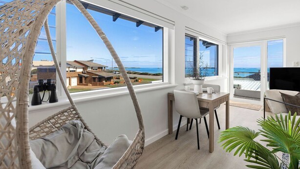 A balcony with a hanging chair, a dining table with chairs, and a TV. - Your Private Coastal Escape | Steps from Shoalwater Beach (Shoalwater)
