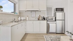 A modern kitchen with white cabinets, a built-in microwave, a refrigerator, and a window with a view. - Sea view Retreat - Spot Dolphins (Shoalwater)