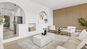 A modern living room with a white sofa, a coffee table, and a dining area visible through an archway. - The Coastal Haven 1BR (Shoalwater)
