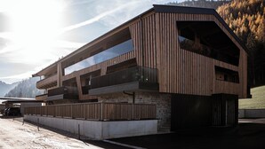 A modern multi-story building with wooden paneling and large glass windows, set against a mountainous backdrop.