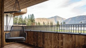 Een houten balkon met een hangstoel, een houten vloer en uitzicht op bergen en bomen.