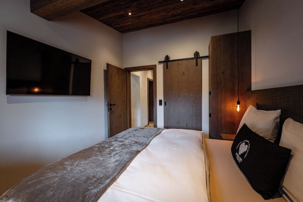 Un dormitorio con una cama grande, cabecera de madera, televisor montado y puerta corredera.