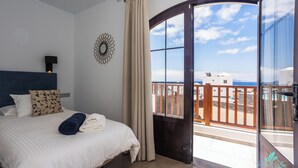 Ein Schlafzimmer mit Bett, Nachttisch, Wanduhr und Blick auf den Strand durch eine Glastür.