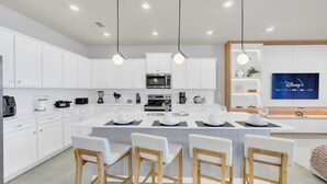 A modern kitchen with white cabinets, a central island with bar stools, a flat-screen TV, and various appliances. - Princess Castle | Avenger Slide | Mario Kart 15985 (Clermont)