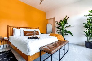 A bedroom with a wooden bed, white bedding, a brown bench, and two potted plants. - Short North Convention King Bed Free Parking (Columbus)