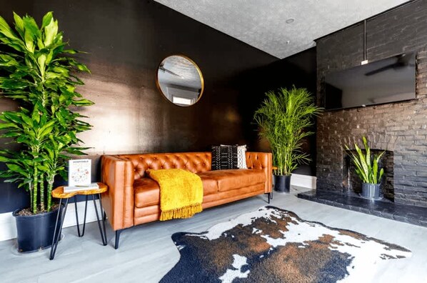 A modern living room with a leather sofa, a round mirror, and potted plants. - Short North Convention King Bed Free Parking (Columbus)