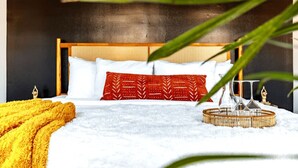 A bed with white bedding, a red patterned pillow, and a yellow throw blanket.