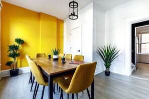 A dining area with a wooden table and yellow chairs, surrounded by potted plants. - Short North Convention King Bed Free Parking (Columbus)