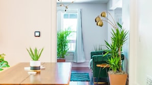 A modern living room with a wooden dining table, green sofa, and potted plants.