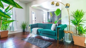 A living room with a teal sofa, a black rug, and multiple potted plants.